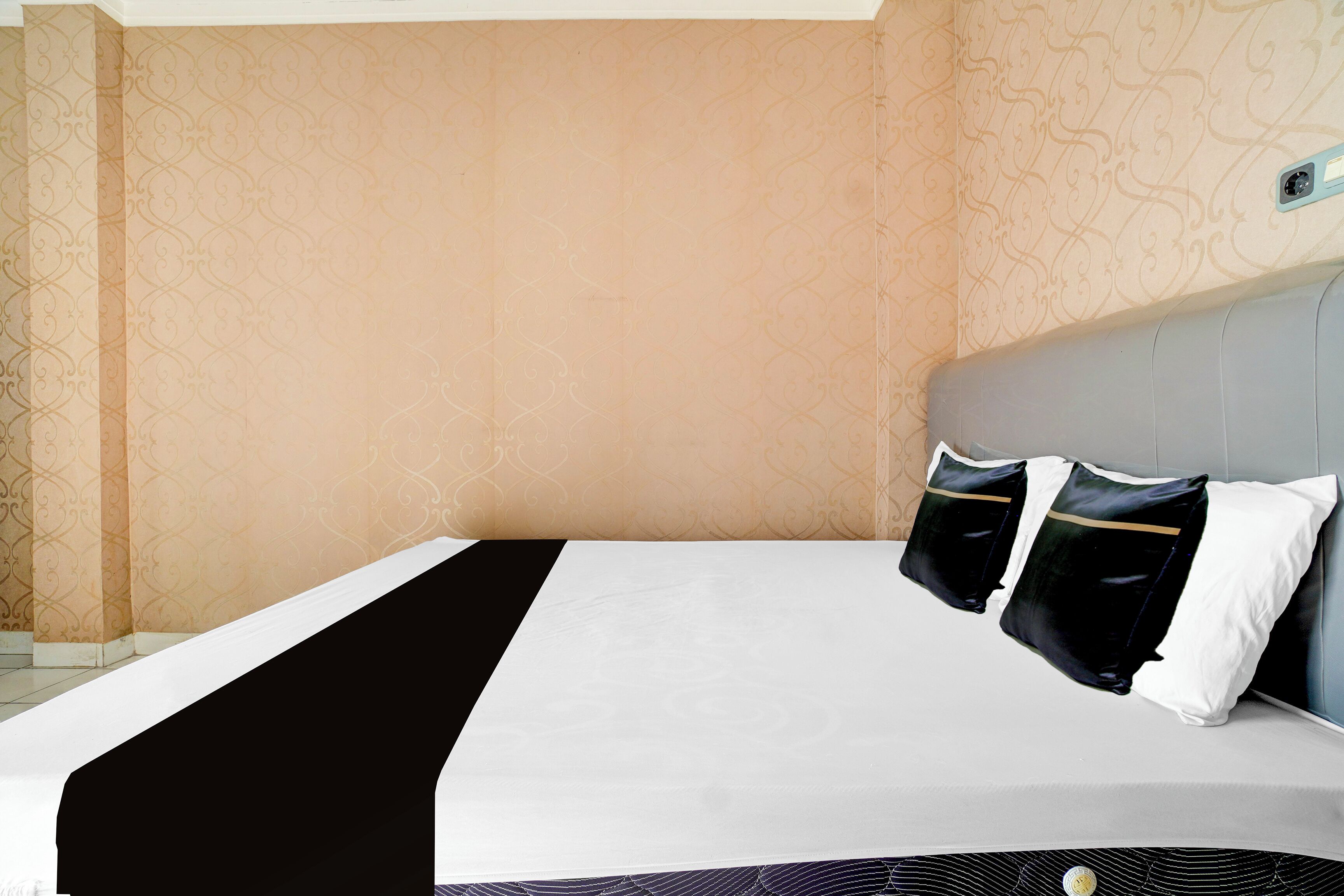 A hotel room with a bed, two pillows, a headboard, and patterned wallpaper.