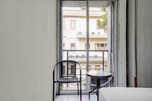 A balcony with a chair and a small table, overlooking a building with multiple windows and balconies. - OYO 92723 Sultan Residence Syariah (Jakarta)