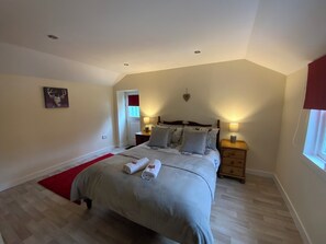 Une chambre à coucher avec un lit, des tables de chevet, un tapis rouge, un tableau et une fenêtre.