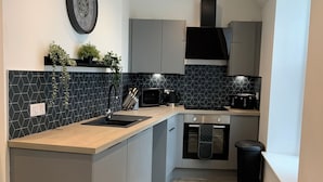 A modern kitchen with a central island, grey cabinets, a black backsplash, and a clock on the wall. - Deeside Snugs (Aboyne)