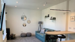 A modern living room with a blue sofa, round mirrors, a small round table, and a bar area. - Deeside Snugs (Aboyne)