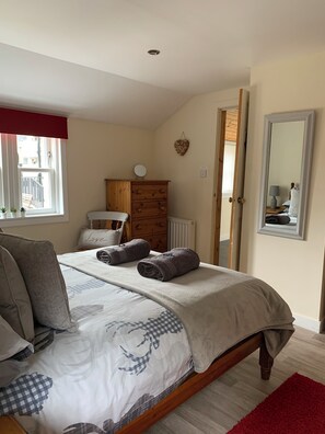 Une chambre à coucher avec un lit, une commode, un miroir et une fenêtre donnant sur des immeubles.