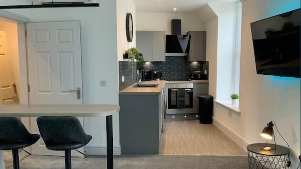 A modern kitchen with a central island, bar stools, and a dining table. - Deeside Snugs (Aboyne)