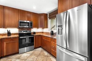 A modern kitchen with wooden cabinets, stainless steel appliances including a refrigerator, oven, and microwave, and a granite countertop. - Keauhou Kona Surf & Racquet 1104: Ocean Views, Resort Amenities & Prime Location (Kailua Kona)