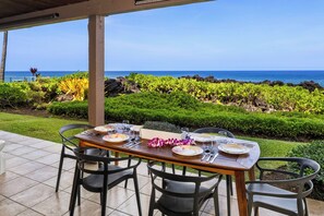 Een terras met een eettafel voor vier personen, met uitzicht op een kustlandschap en de oceaan.
