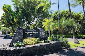 A sign for Keauhou Kona Surf and Racquet Club with a stone wall and tropical plants. - Keauhou Kona Surf & Racquet 1104: Ocean Views, Resort Amenities & Prime Location (Kailua Kona)