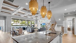 Une cuisine moderne dotée d’un grand îlot central, de luminaires suspendus et offrant une vue sur l’extérieur.