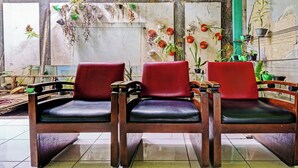 Trois chaises en bois avec des coussins noirs, dans une pièce dont le sol est recouvert de carreaux et dont un mur est décoré de différents pots de plantes.
