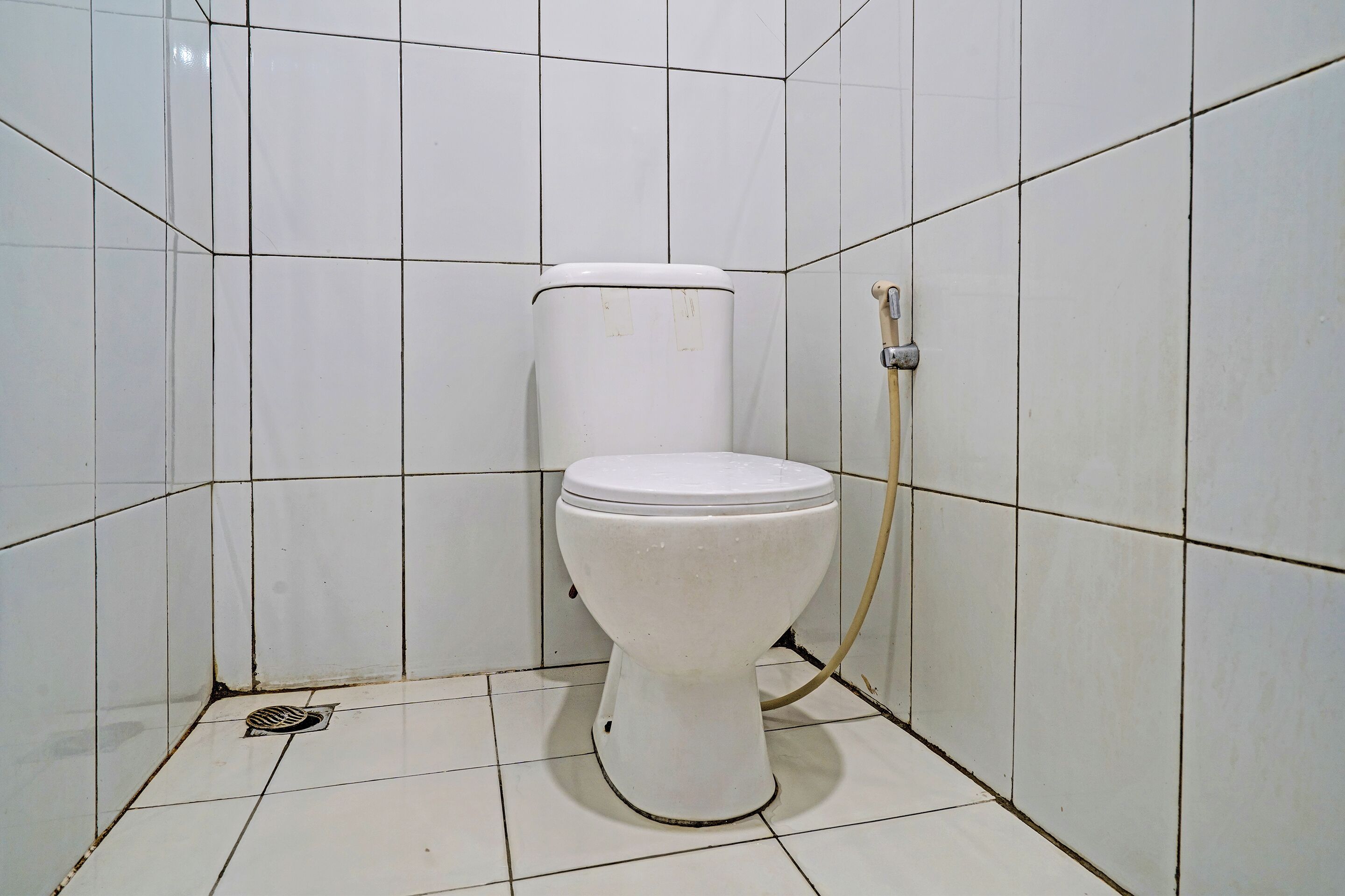 A small, white toilet in a tiled bathroom with a visible drain and a water pipe.