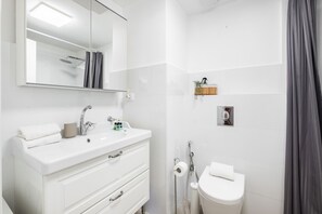 Uma casa de banho moderna com lavatório branco, um espelho grande, chuveiro e sanita.