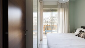 Een hotelkamer met een bed, een balkon met een stoel en uitzicht op gebouwen.