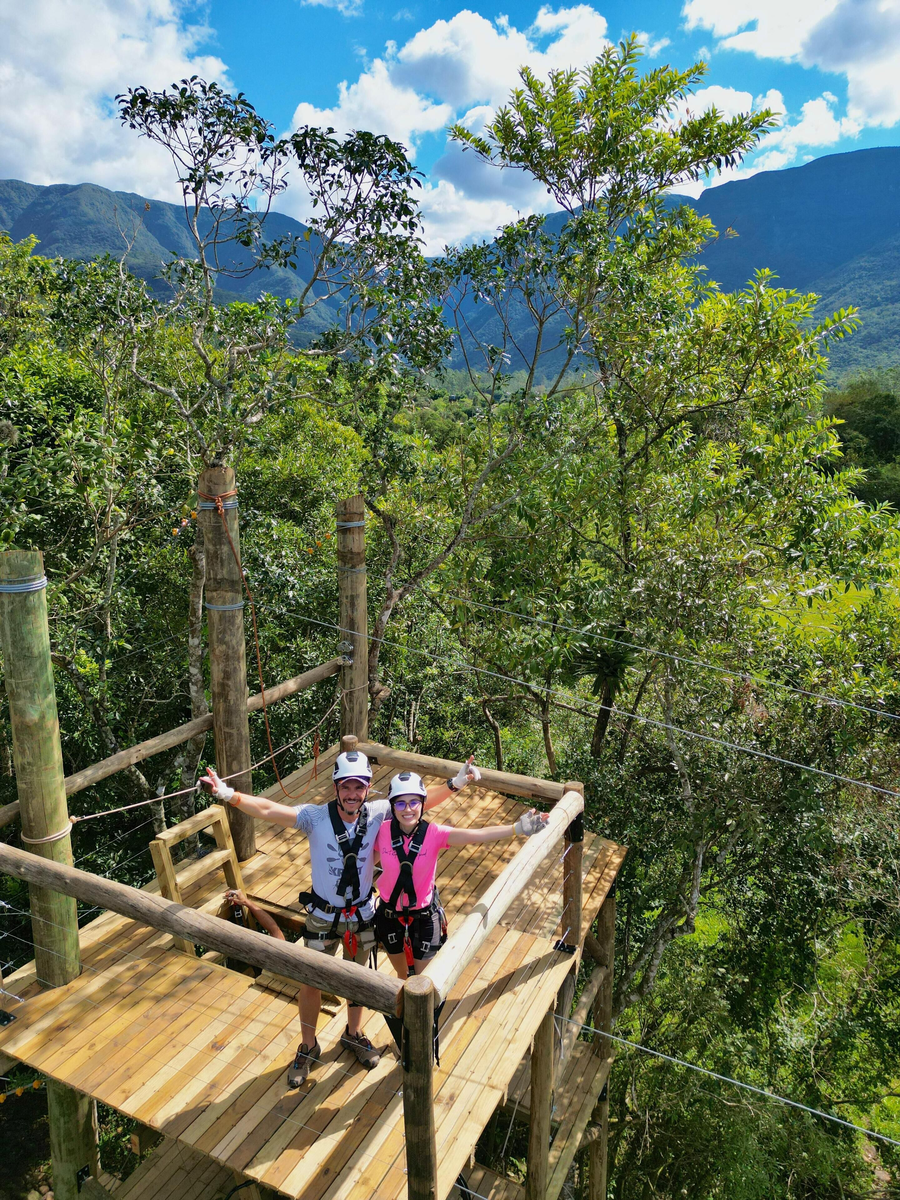 A wooden platform with railings, surrounded by lush greenery and mountains in the background.