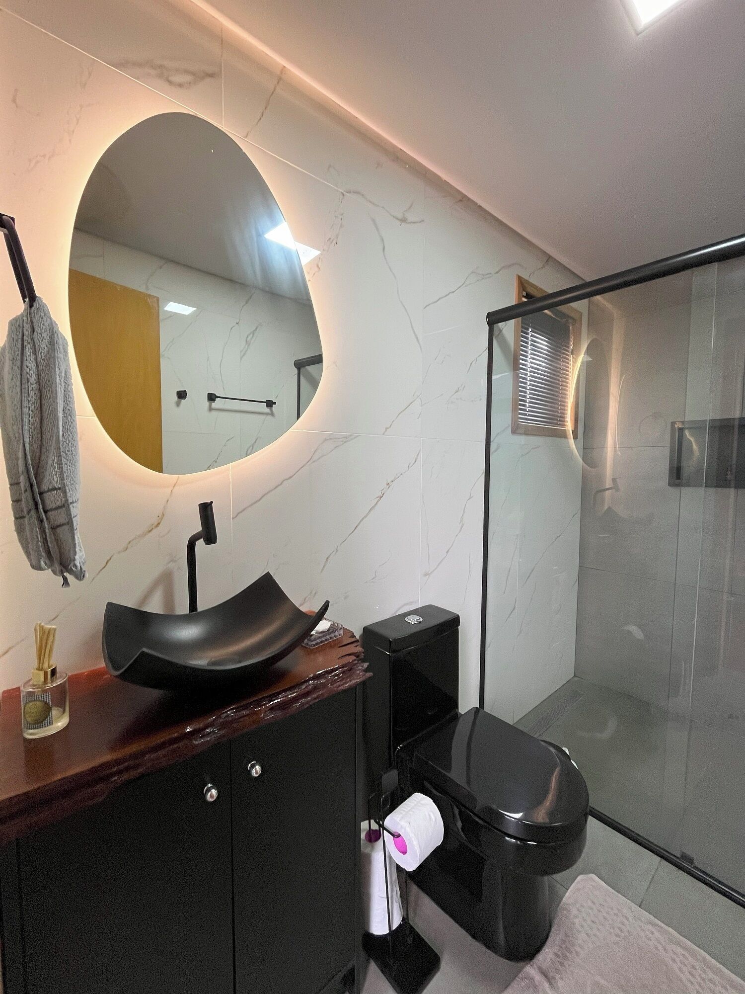 A modern bathroom with a round mirror, a black sink, a toilet, and a glass shower enclosure.