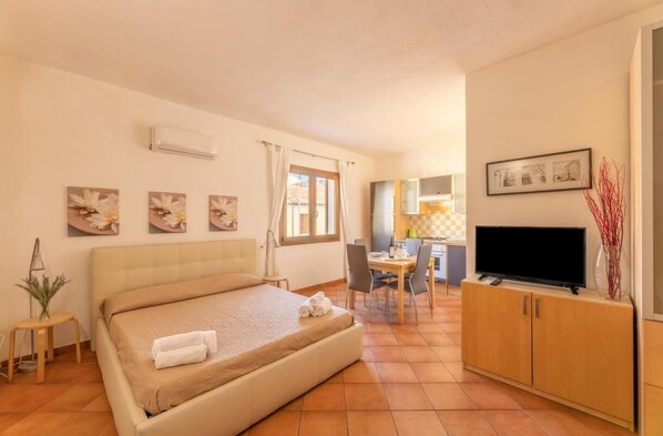 A hotel room with a bed, a desk, a TV, and artwork on the walls.