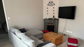 A living room with a grey sectional sofa, a wooden coffee table, a fireplace, and a flat-screen TV mounted on the wall.