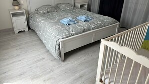 A bedroom with a bed, nightstands, a crib, and a lamp.