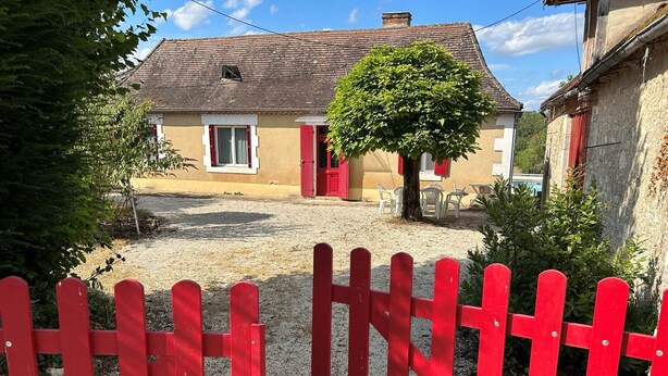 A house with a red door, a tree in front, and a gravel driveway.