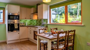 A kitchen with a dining table and chairs, a window with a view of greenery, and a hanging light fixture.