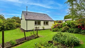 A single-story house with a sloped roof, a small garden with various plants and flowers, and a clear blue sky.