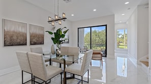 A modern dining area with a glass table, cushioned chairs, and a chandelier.