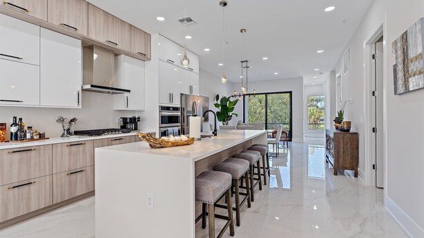 A modern kitchen with a central island, bar stools, and a large window providing a view of the outdoors. - Uptown Luxury On Audubon 4 Bedroom Townhouse by RedAwning (Sarasota)