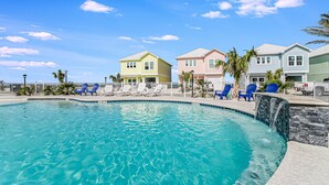 A swimming pool with clear blue water, surrounded by a white fence. There are several colorful houses in the background. - Birds Eye View Sp163 3 Bedroom Home by RedAwning (Rockport)