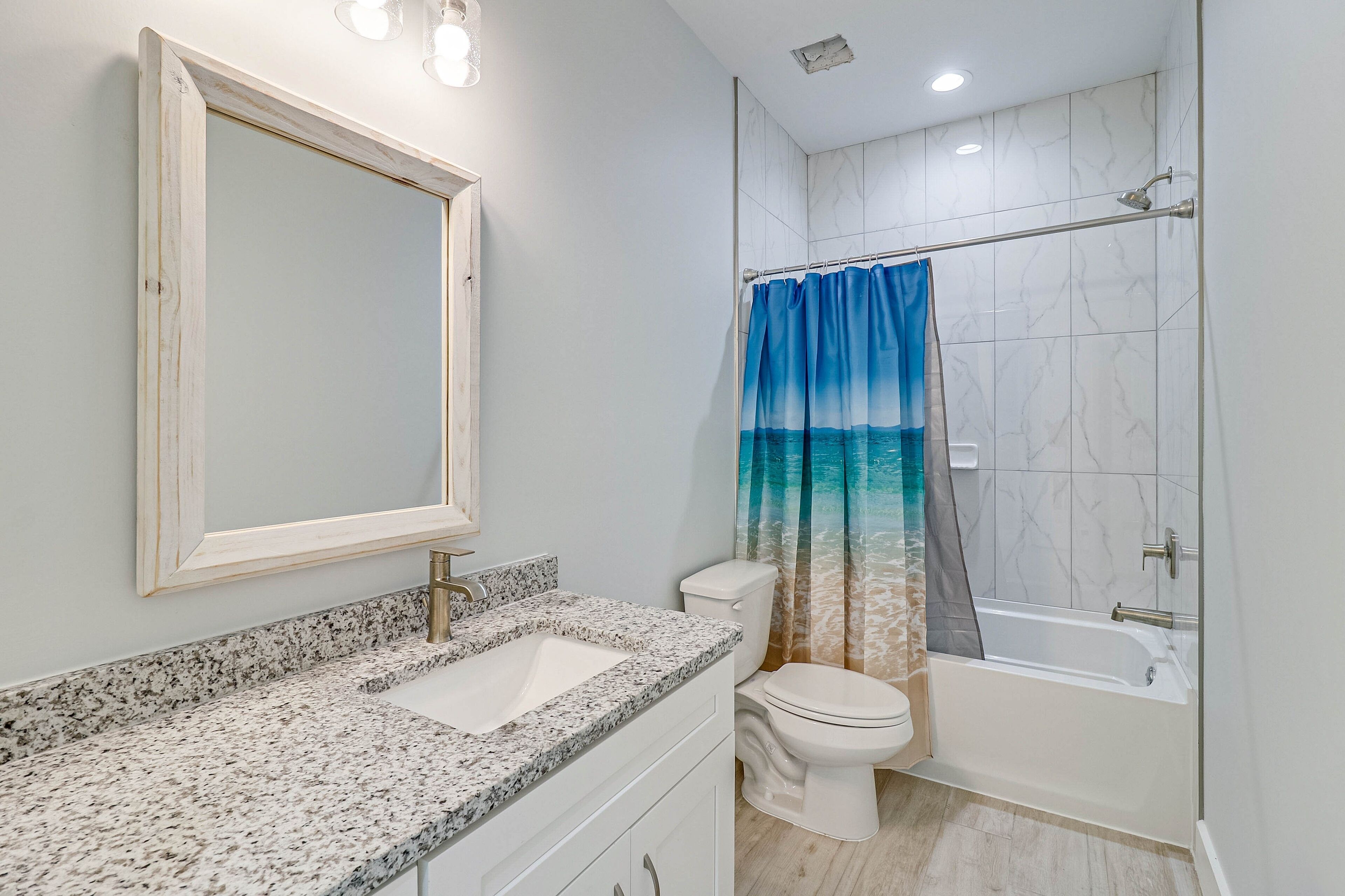 A bathroom with a granite countertop sink, a white toilet, a bathtub, and a shower curtain with a blue gradient.