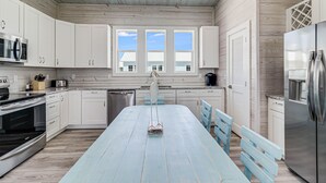 A modern kitchen with white cabinets, a large island, stainless steel appliances, and a view of the outside through windows. - Birds Eye View Sp163 3 Bedroom Home by RedAwning (Rockport)