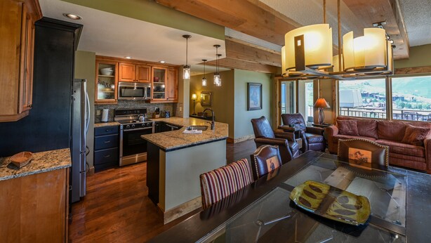 A spacious kitchen with granite countertops, wooden cabinets, and a large island. There is a dining area with a glass table and leather chairs.