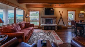 A cozy living room with a fireplace, leather furniture, and a large window overlooking a scenic view.