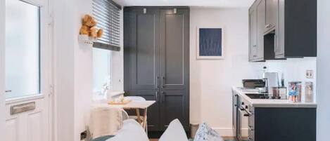 Une chambre d’hôtel compacte comprenant un lit, une petite table avec une chaise, une kitchenette et une grande armoire.