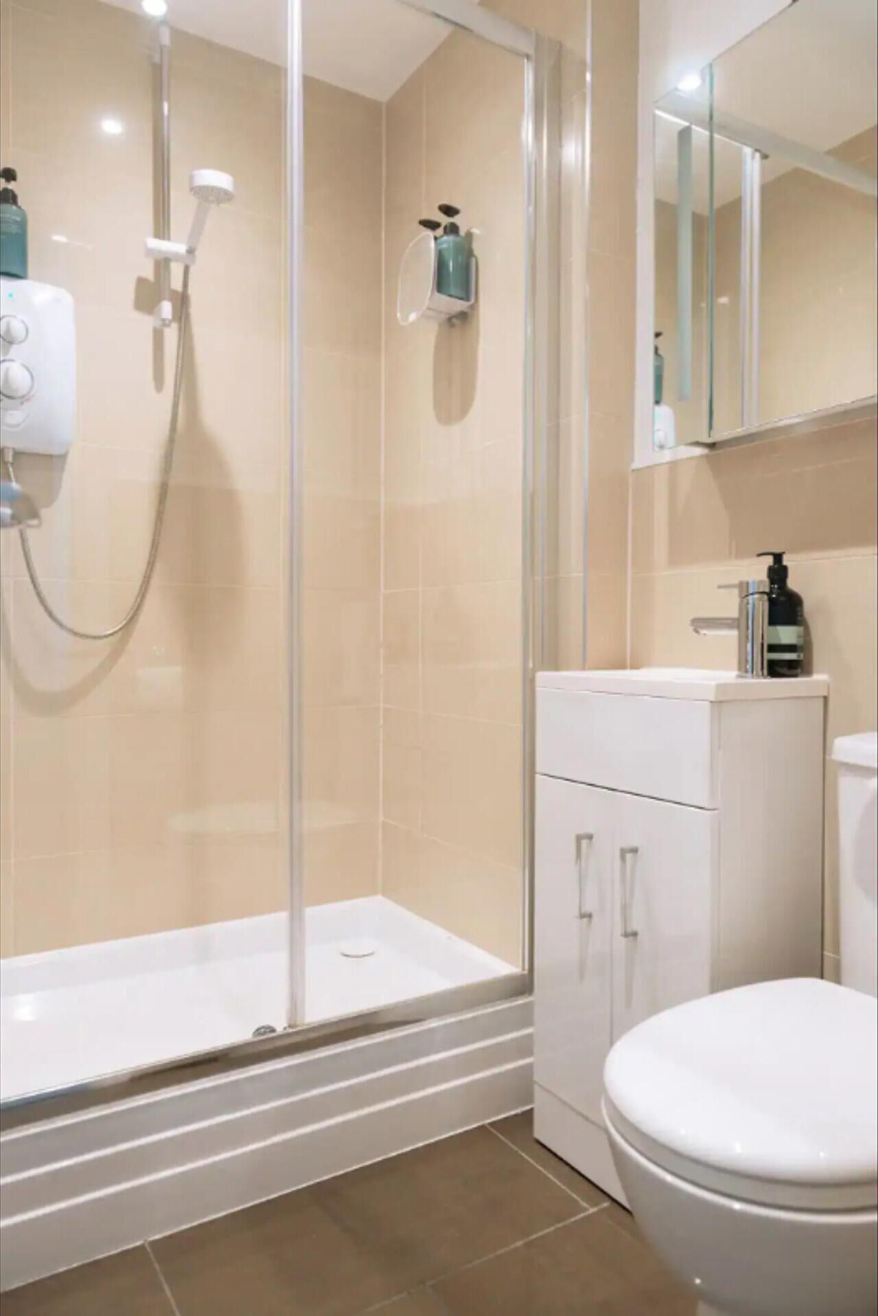 Een moderne badkamer met een douchecabine van glas, een witte wastafel en een toilet.