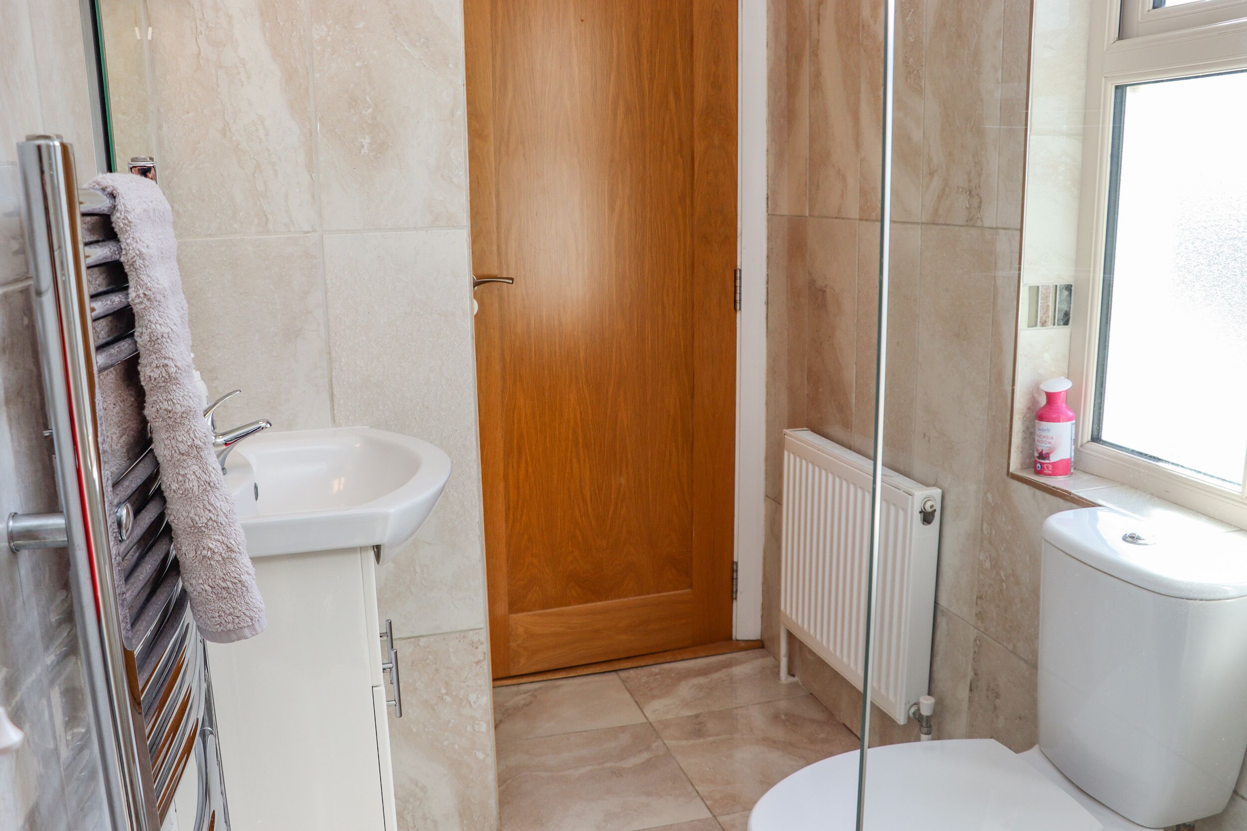 Un baño con puerta de madera, lavamanos blanco y un inodoro.