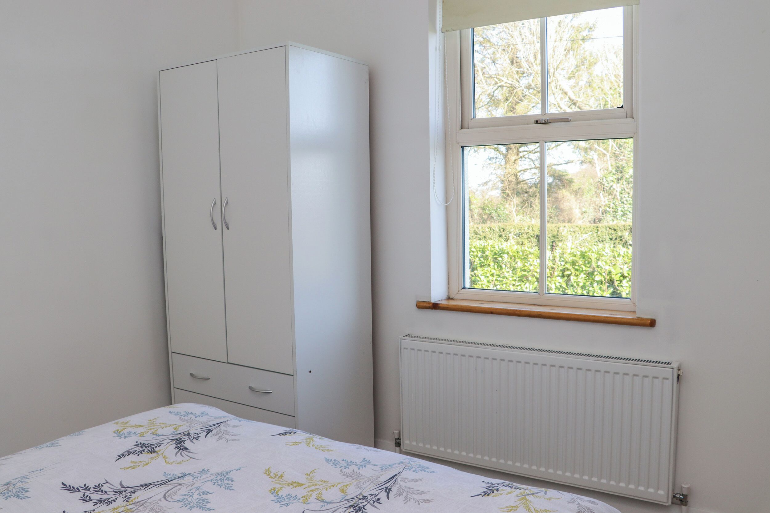 Una camera da letto con un letto, un armadio, una finestra con vista sul verde e un termosifone.