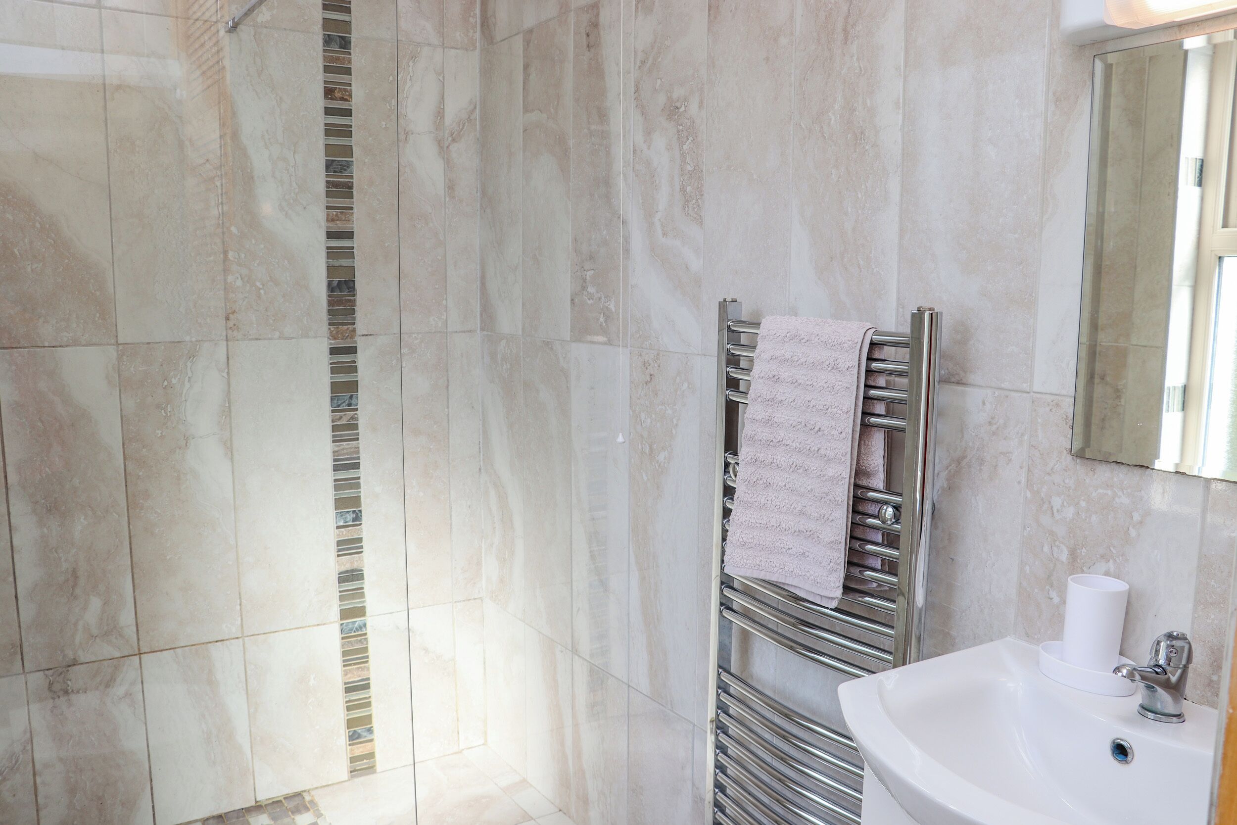 A bathroom with a marble wall, a towel rack with a towel, and a sink with a mirror.