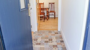 A hallway with patterned flooring leading to a dining area with wooden chairs and a table. - An Teachain (Adamstown)