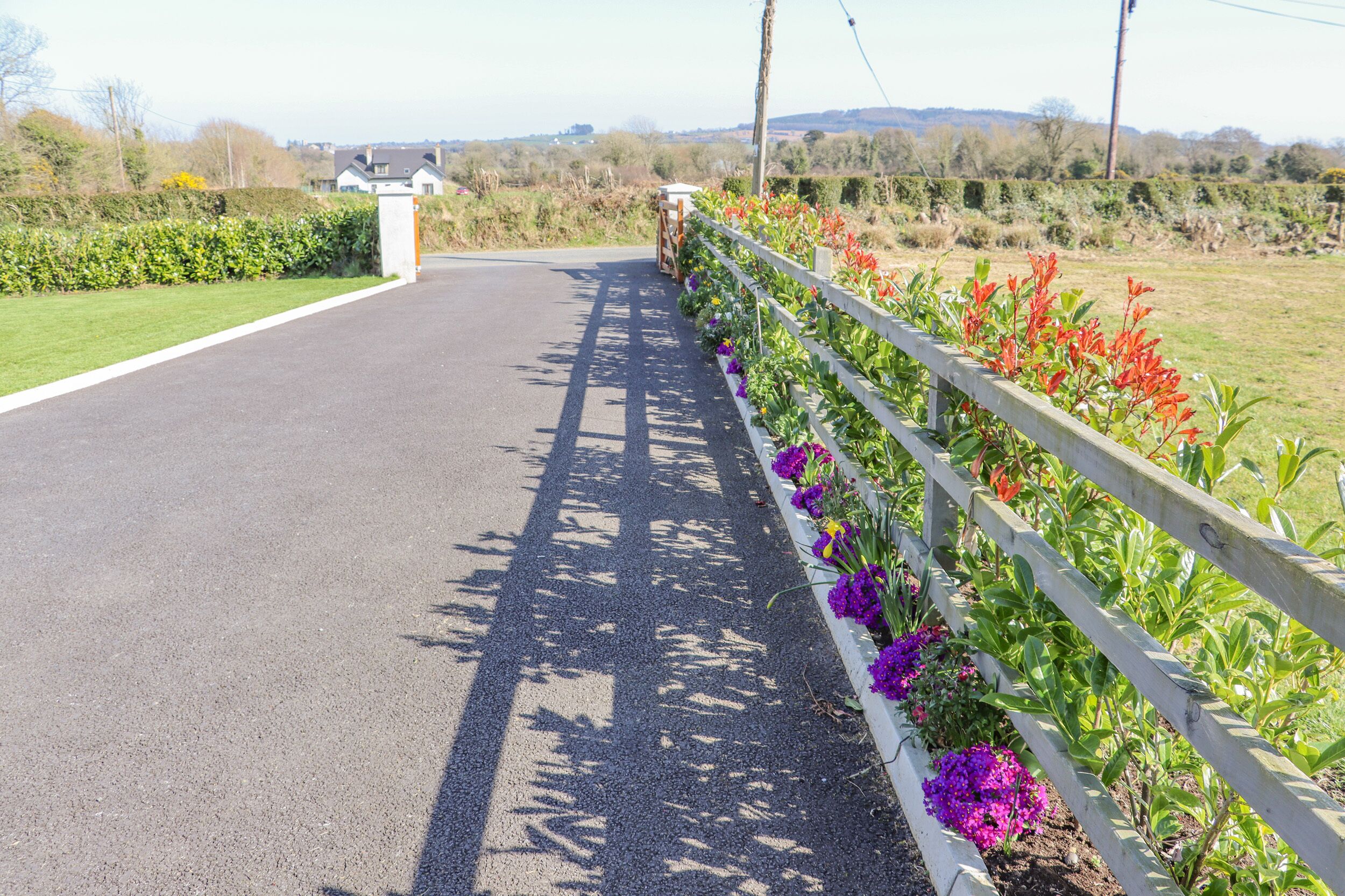 A paved road with a white fence and flower beds on one side.