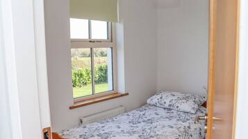 A small bedroom with a single bed, a window with a view of greenery, and a ceiling light.