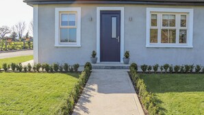 A two-story house with a dark blue front door, white-framed windows, and a tiled roof. - An Teachain (Adamstown)