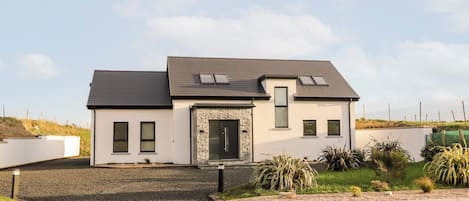 A modern two-story house with a stone entrance, multiple windows, and a sloped roof.
