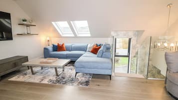Een moderne woonkamer met een hoekbank, een salontafel en een televisie. Er zijn dakramen en uitzicht op de omgeving.