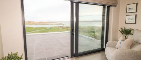 Sala moderna com uma grande porta de correr de vidro que dá para uma varanda com vista para um lago e colinas ao longe.