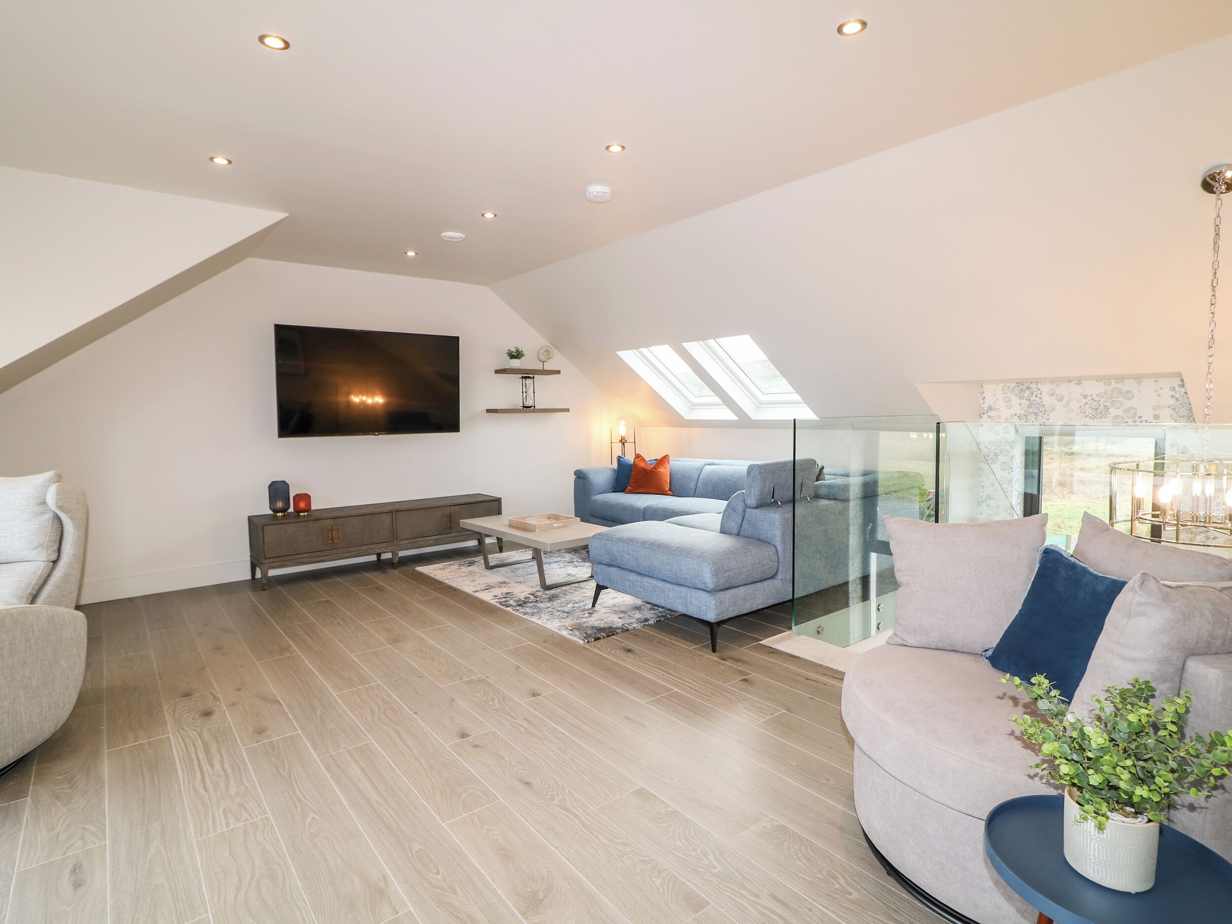 Una sala de estar moderna con un televisor de pantalla plana grande, un sofá modular, una mesa de centro de vidrio y piso de madera.