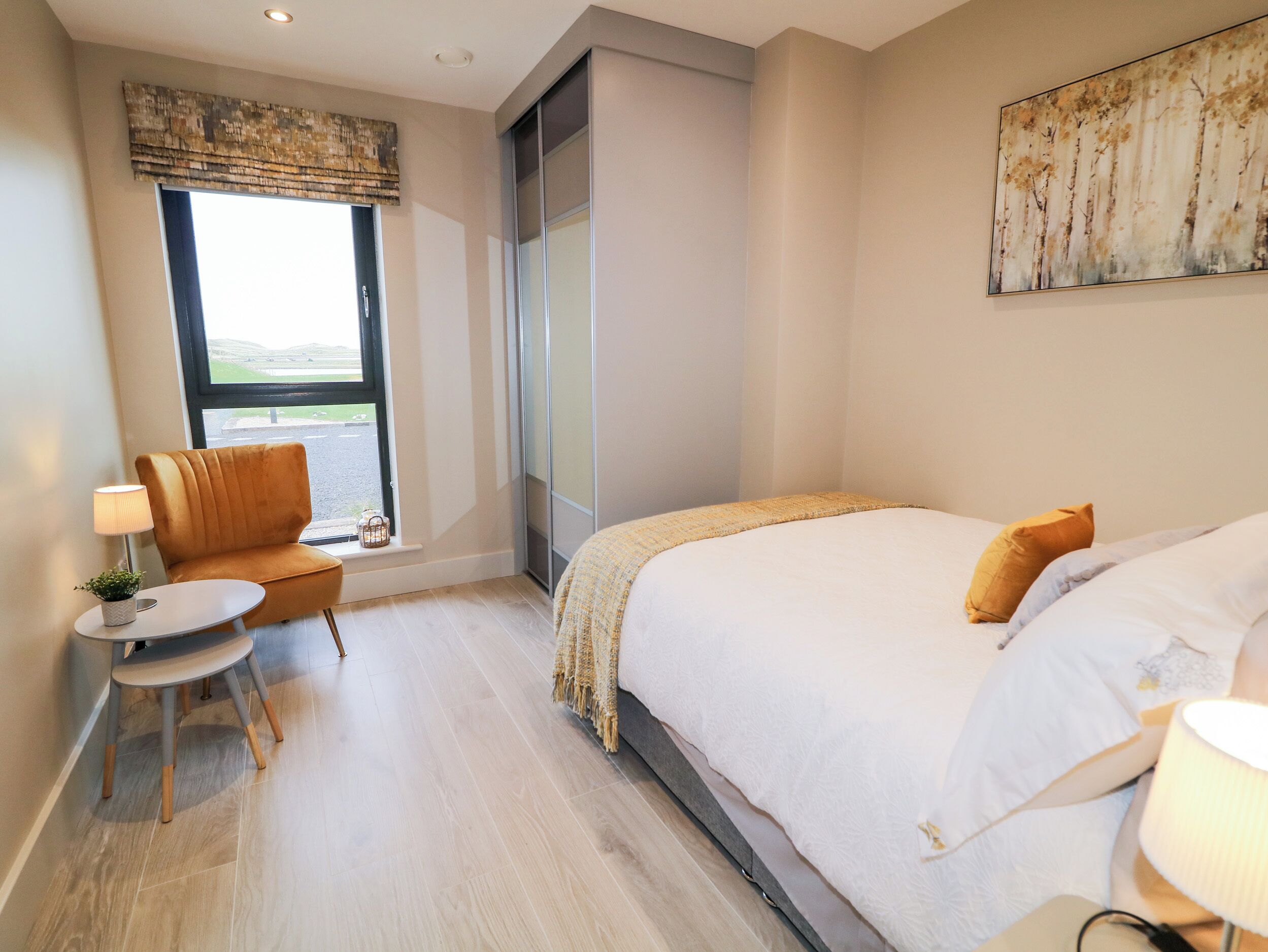 Ein modernes Hotelzimmer mit einem großen Bett, einem kleinen Tisch mit Lampe, einem Sessel und einem großen Fenster mit Blick.