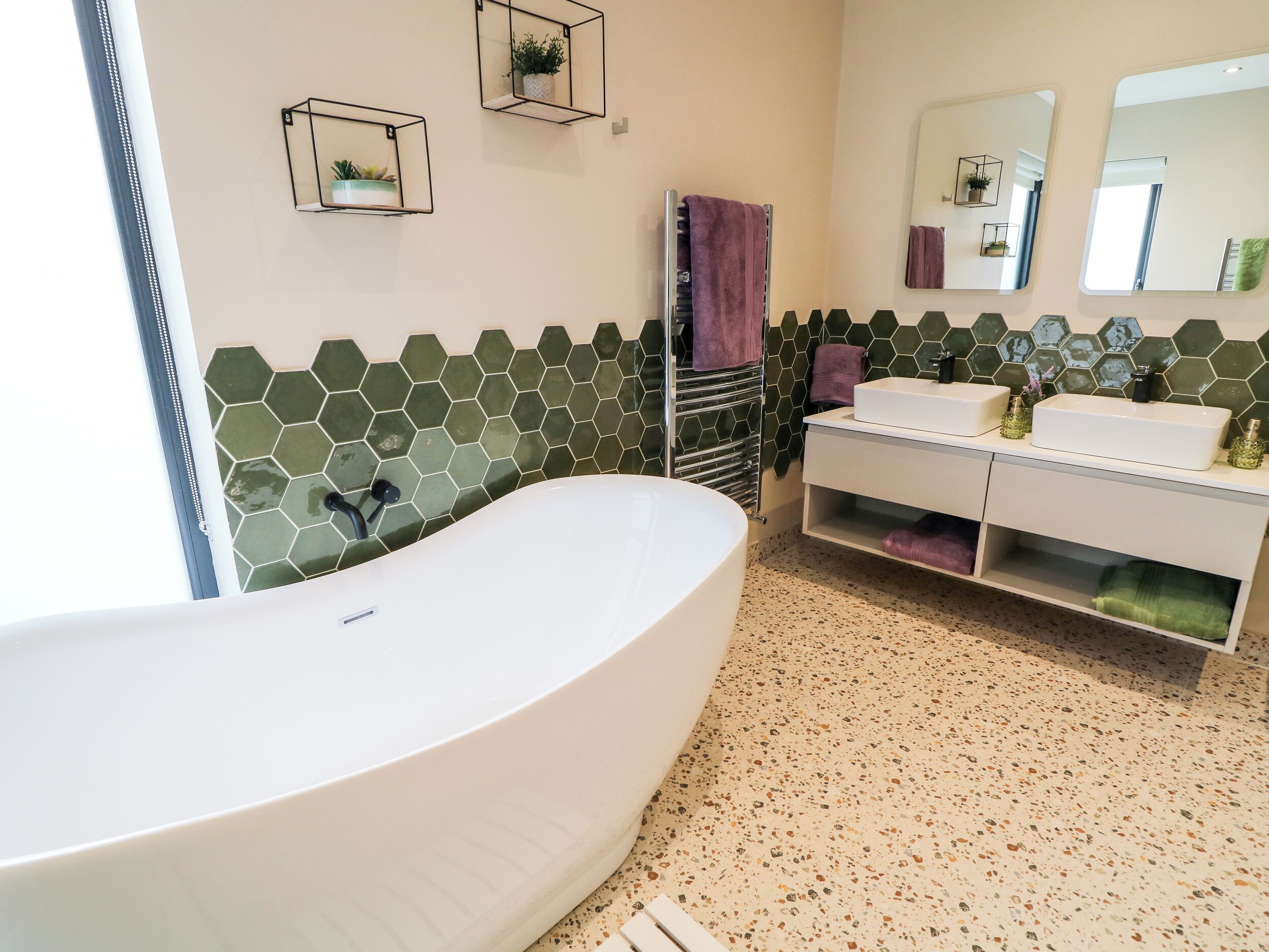 A modern bathroom with a freestanding bathtub, a vanity with a mirror, and a hexagonal tile backsplash.