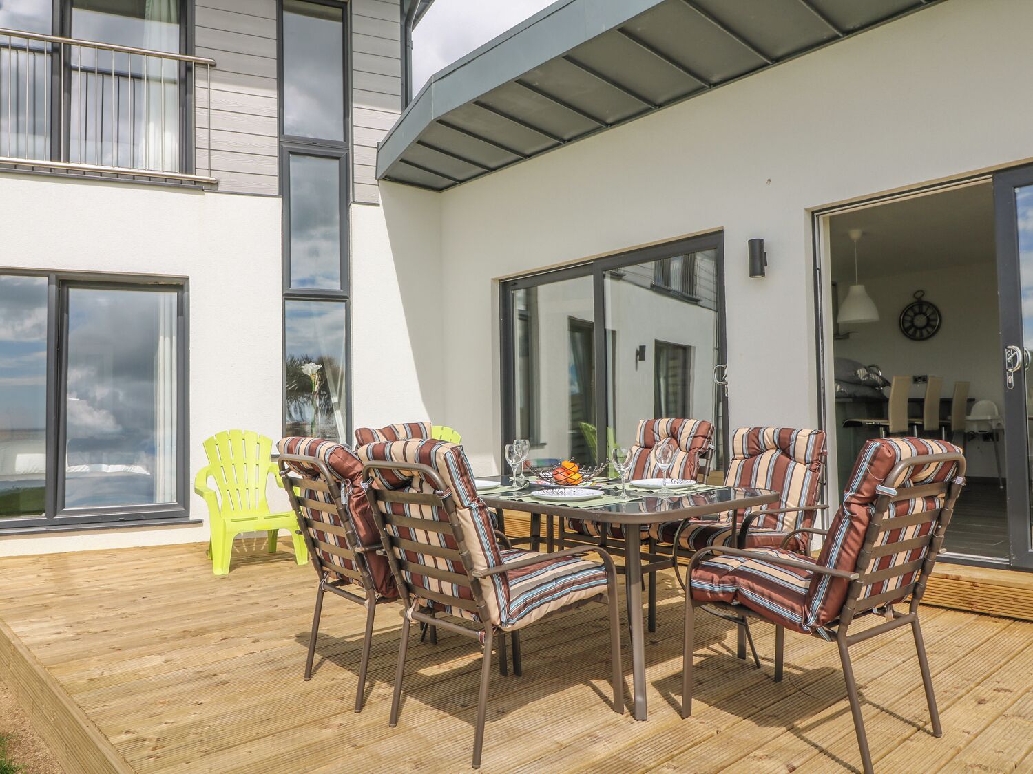 Eine Terrasse im Freien mit einem runden Tisch und Stühlen, ein leuchtend gelber Stuhl und eine Schiebetür zu einem Innenbereich.