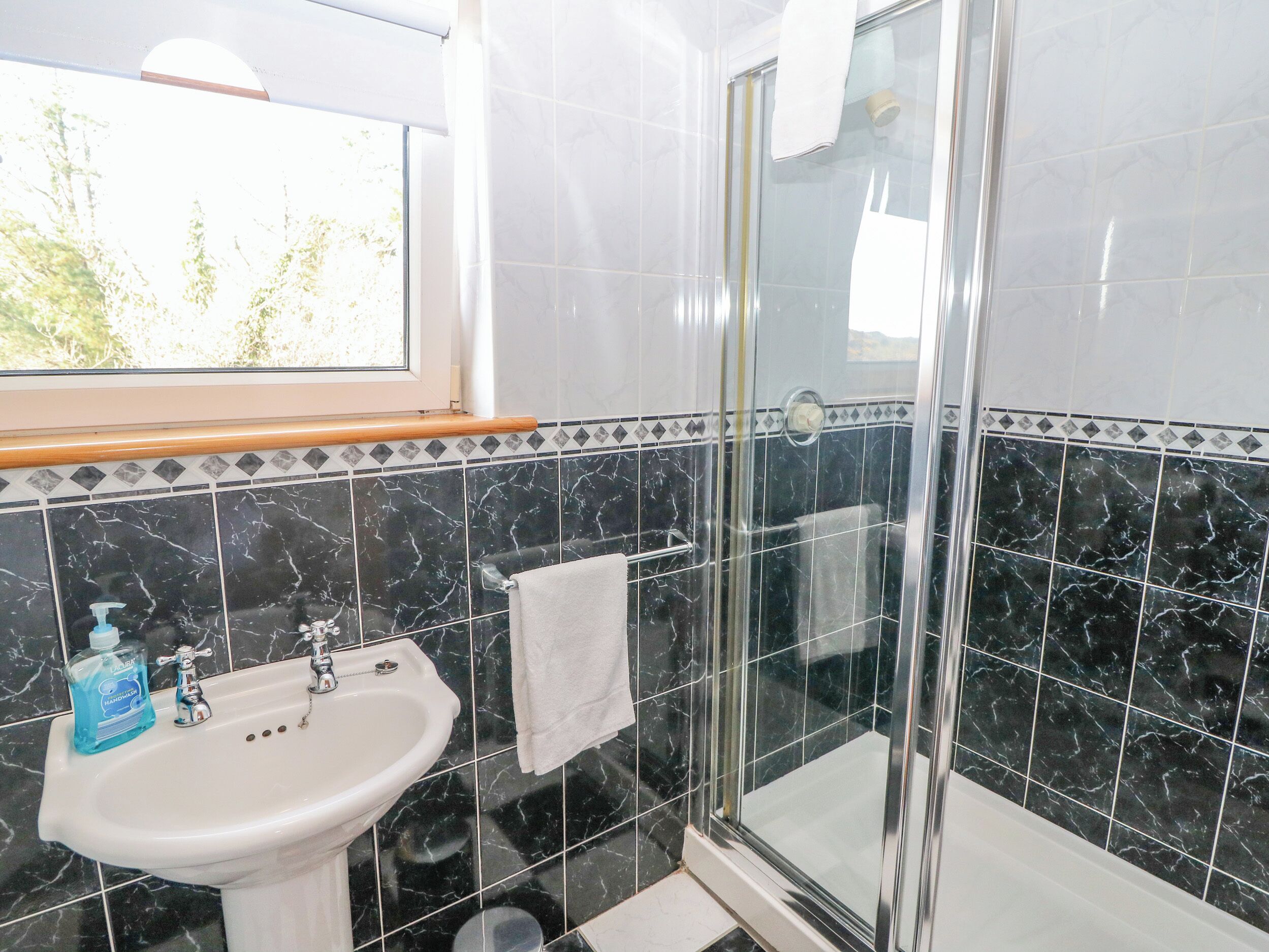 A bathroom with a glass shower, a sink, and a window.