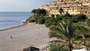Un hôtel situé sur la côte, doté de nombreux balcons, d’une plage de sable et d’une végétation luxuriante.