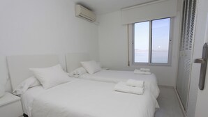 Une chambre d’hôtel avec deux lits, une table de chevet, un appareil de climatisation, une fenêtre avec vue et une porte à persiennes.