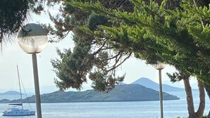 Un jardin agrémenté de plantes en pot, une pelouse et une vue sur un plan d’eau où l’on aperçoit un voilier.